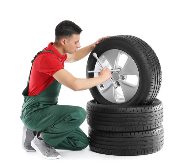 Jovem mecânico masculino em uniforme com pneus de carro e chave cruzada no fundo branco — Fotografia de Stock