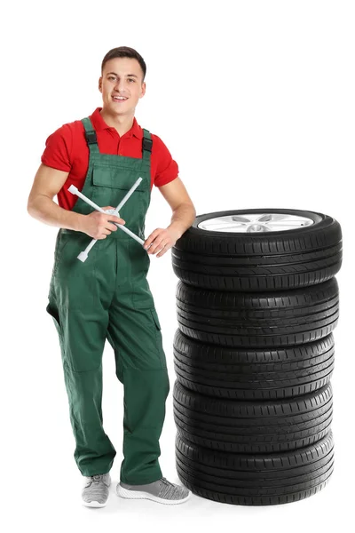 Joven mecánico en uniforme con neumáticos de coche y llave cruzada sobre fondo blanco —  Fotos de Stock