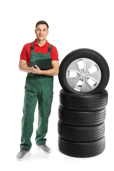 Jeune mécanicien masculin en uniforme avec des pneus de voiture sur fond blanc — Photo