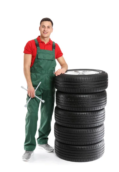 Jovem mecânico masculino em uniforme com pneus de carro e chave cruzada no fundo branco — Fotografia de Stock
