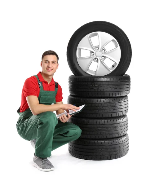 Jovem mecânico masculino em uniforme com pneus de carro no fundo branco — Fotografia de Stock