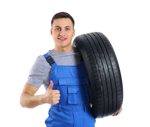 Joven mecánico masculino con neumático de coche mostrando gesto de pulgar hacia arriba sobre fondo blanco — Foto de Stock