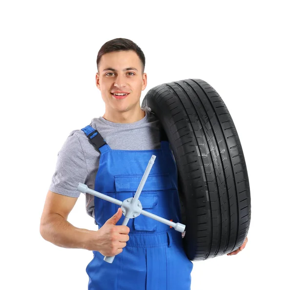 Jovem mecânico masculino em uniforme com pneu de carro e chave cruzada no fundo branco — Fotografia de Stock