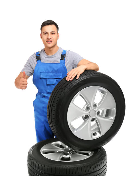 Young male mechanic with car tires showing thumb-up gesture on white background