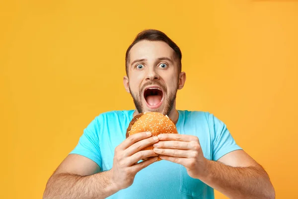 Man with burger on color background — Stock Photo, Image