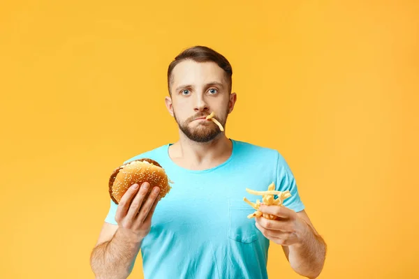 Homem com hambúrguer e batatas fritas no fundo da cor — Fotografia de Stock