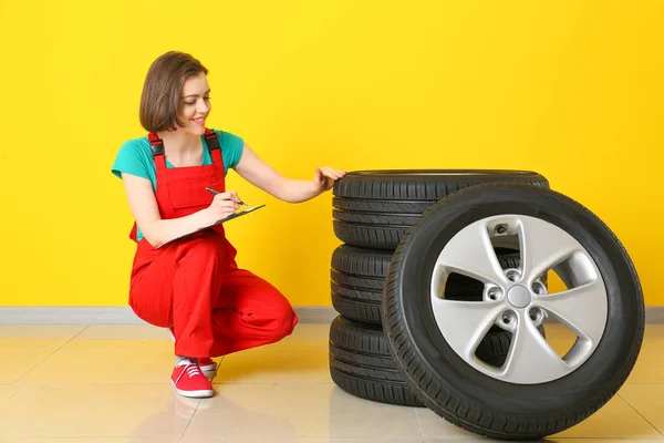 Jovem mecânica feminina em uniforme e com pneus de carro perto da parede de cor — Fotografia de Stock