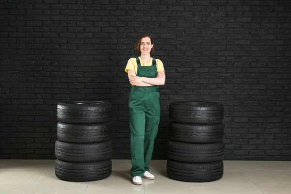 Młoda kobieta mechanik w mundurze i z opon samochodowych przed ciemną ścianę — Zdjęcie stockowe