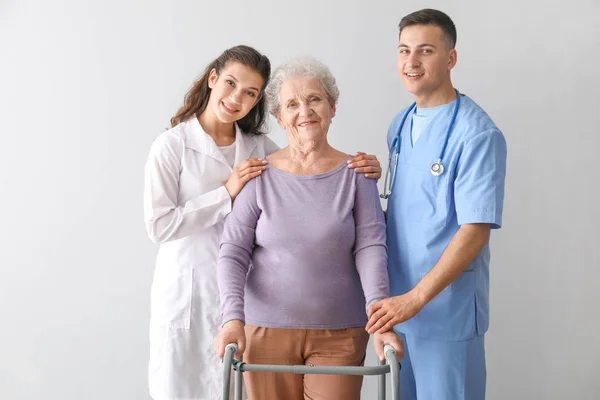 Young medical workers with senior woman on grey background — Stock Photo, Image