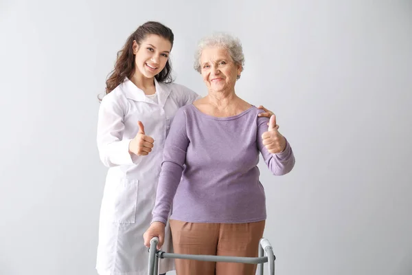 Jovem médico com mulher sênior mostrando gesto de polegar para cima em fundo cinza — Fotografia de Stock