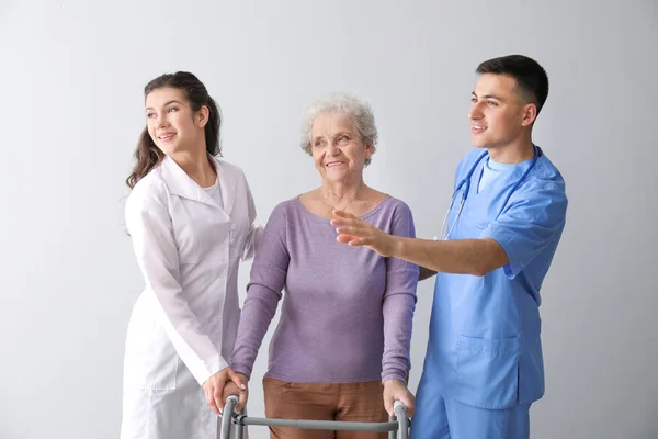 Młodzi pracownicy medyczni ze starszym kobietą na szarym tle — Zdjęcie stockowe
