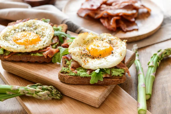 Tasty toasts with bacon and fried egg on wooden board — Stock Photo, Image