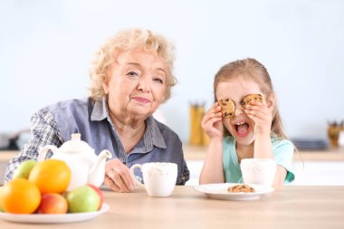 Sevimli küçük kız ve büyükanne mutfakta kurabiye ile çay içme