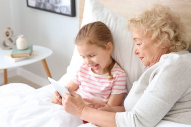 Evde yatakta tablet Pc kullanarak büyükanne ile Sevimli küçük kız