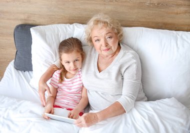 Evde yatakta tablet Pc kullanarak büyükanne ile Sevimli küçük kız