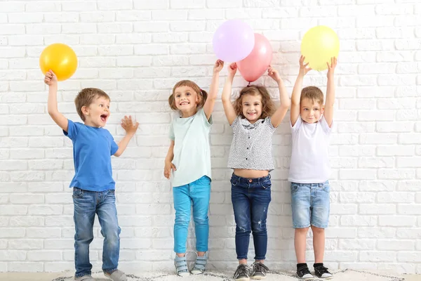 Lindos niños pequeños con globos de aire cerca de la pared de ladrillo blanco —  Fotos de Stock