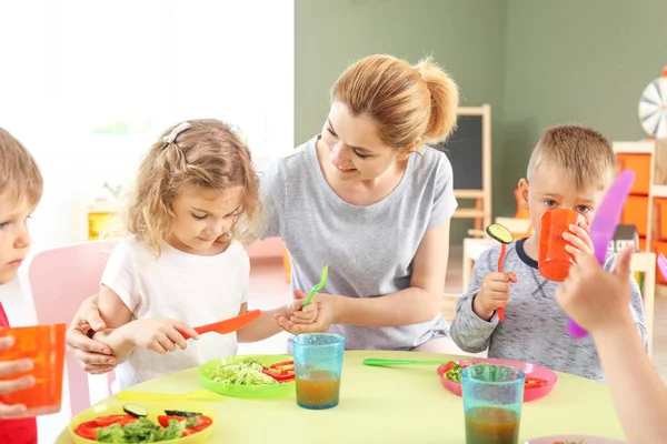 Nursery teacher with cute little children during lunch in kindergarten — Stock Photo, Image