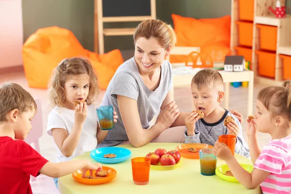 Nursery teacher with cute little children during lunch in kindergarten — Stock Photo, Image