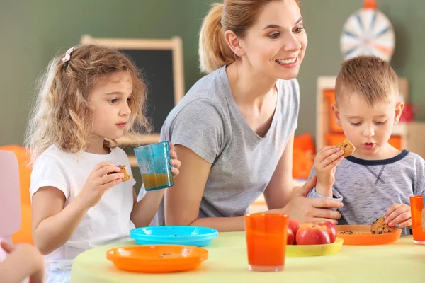 Nursery teacher with cute little children during lunch in kindergarten — Stock Photo, Image