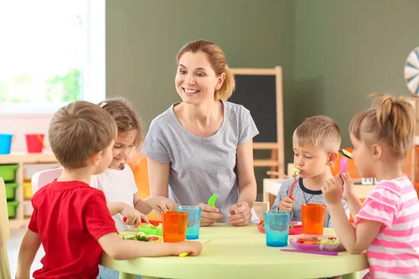 Преподаватель детского сада с милыми детьми во время обеда в детском саду — стоковое фото