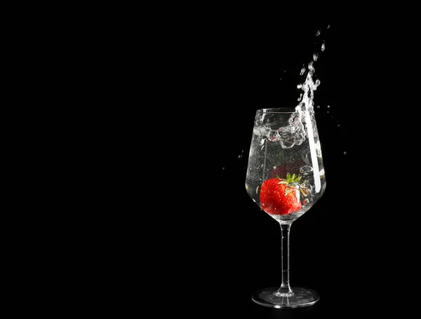 Glass of splashing drink with red strawberry on dark background