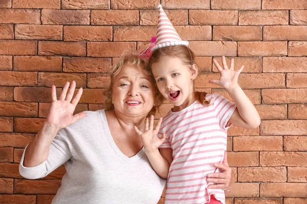 レンガの背景にパーティーの帽子で祖母と幸せな小さな女の子 — ストック写真