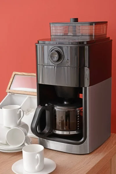 Modern coffee machine and cups on table against color background — Stock Photo, Image