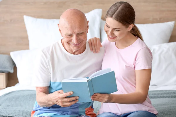 Giovane donna che legge libro con suo padre in casa di cura — Foto Stock