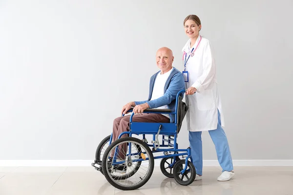 Elderly man in wheelchair and doctor near light wall — Stock Photo, Image