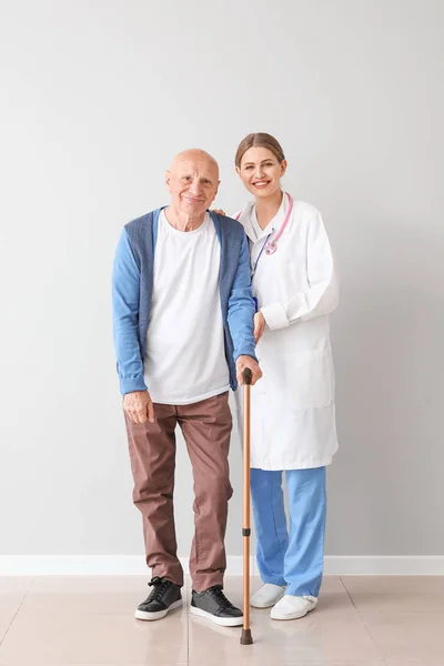 Elderly man with doctor near light wall — Stock Photo, Image
