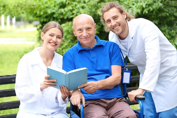 Elderly man with caregivers reading book in park — Stock Photo, Image