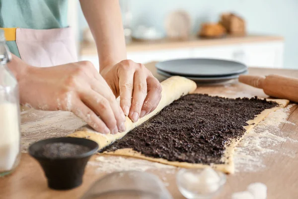 Mujer preparando sabrosa pastelería con semillas de amapola en la mesa —  Fotos de Stock