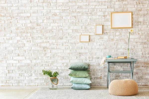 Mesa, pufe e travesseiros macios perto da parede de tijolo — Fotografia de Stock