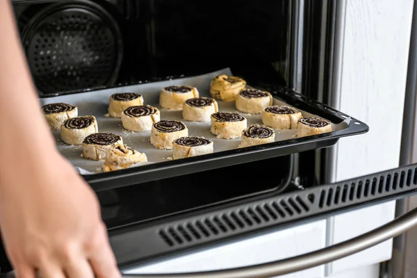 Woman putting baking sheet with raw poppy buns into oven