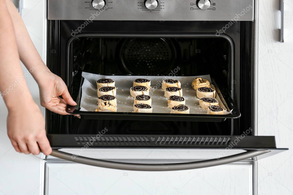 Woman putting baking sheet with raw poppy buns into oven