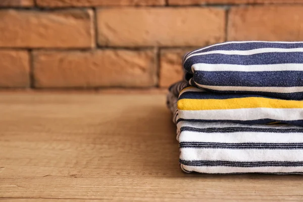 Stack of clothes on table against brick wall — Stock Photo, Image