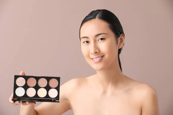 色の背景に化粧を輪郭を描く化粧品を持つアジアの女性 — ストック写真