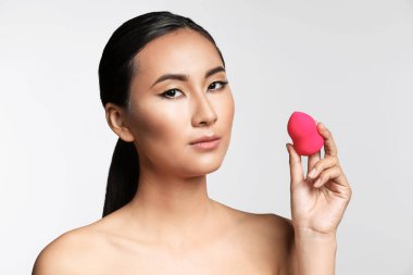 Açık arka plan üzerinde güzel makyaj ve sünger ile Asyalı kadın