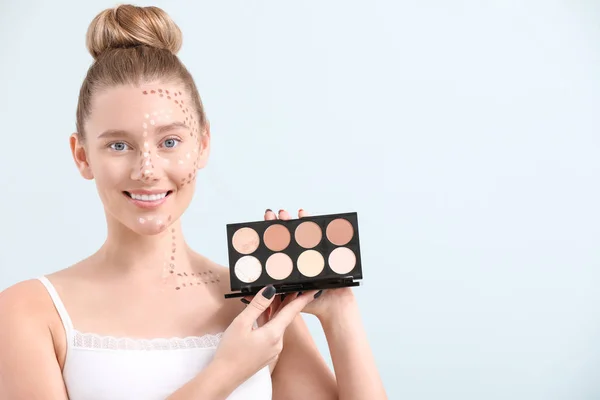 Ung kvinna med kosmetika för contouring makeup på ljus bakgrund — Stockfoto