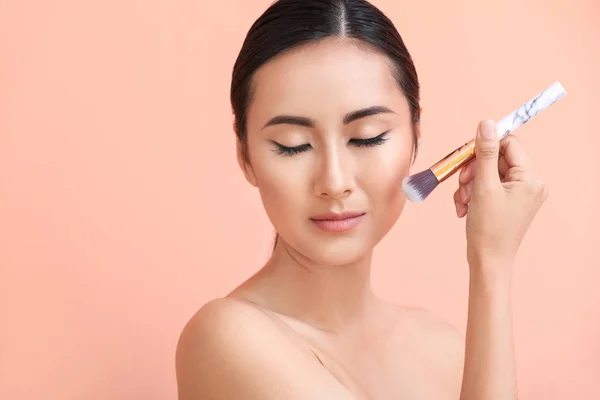 Asian woman with beautiful makeup and brush on color background