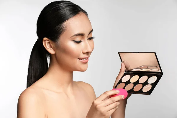 Asian woman with cosmetics for contouring makeup on light background — Stock Photo, Image
