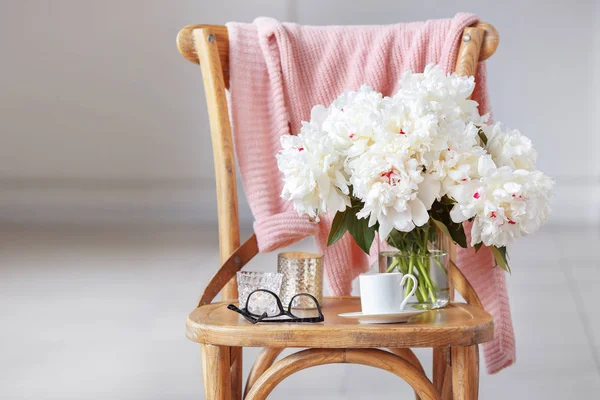 Beautiful peony flowers, candles, cup of coffee and glasses on chair — Stock Photo, Image