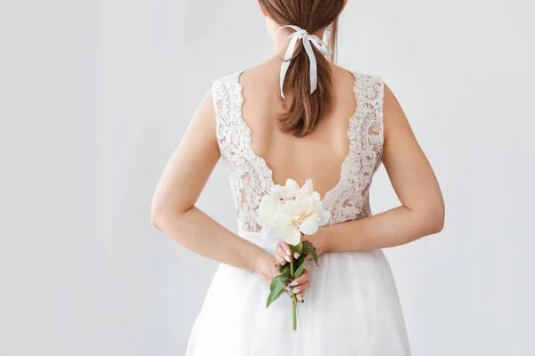 Young bride with beautiful peony on light background, back view — Stock Photo, Image