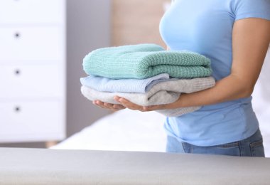 Evde ütü tahtası yakınında duran temiz giysi yığını ile genç kadın