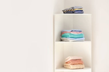 Beyaz duvara yakın temiz giysi yığınları ile Raf