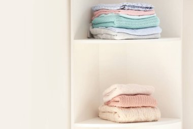 Beyaz duvara yakın temiz giysi yığınları ile Raf