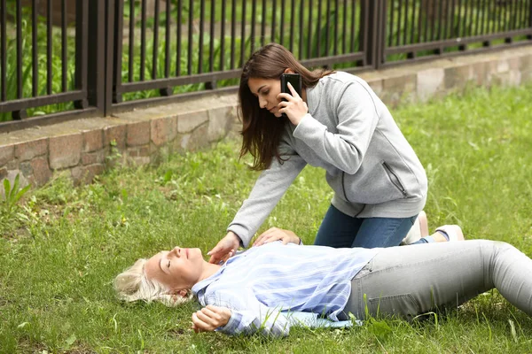 Female passer-by calling an ambulance for unconscious mature woman outdoors — Stock Photo, Image