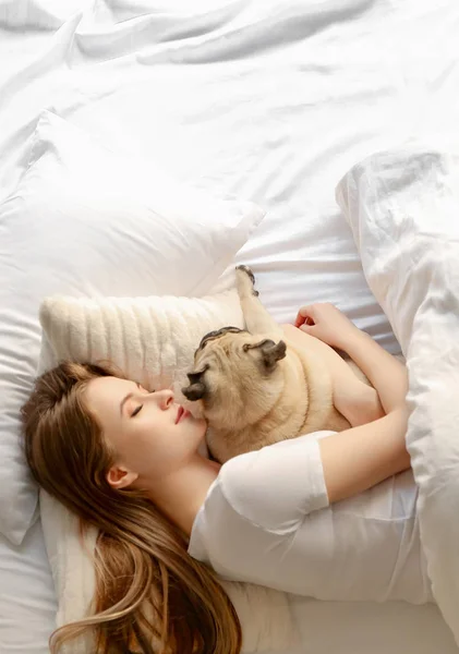 Morning of beautiful young woman with cute pug dog in bedroom — Stock Photo, Image