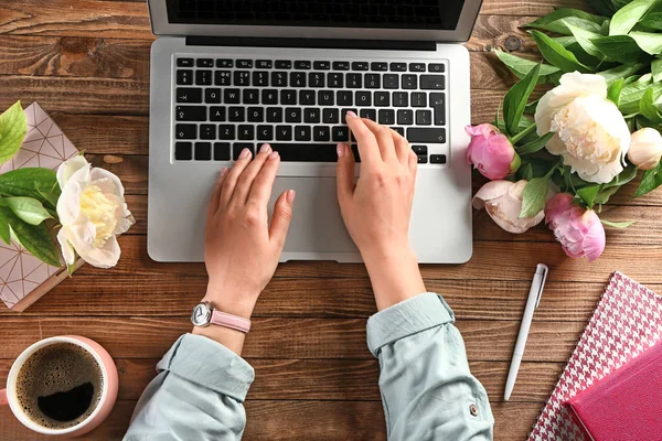 Mujer sentada a la mesa con portátil y ramo de peonías — Foto de Stock