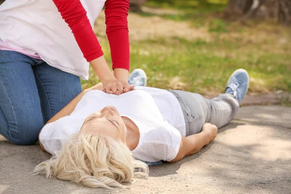 Female passer-by doing CPR on unconscious mature woman outdoors — Stock Photo, Image